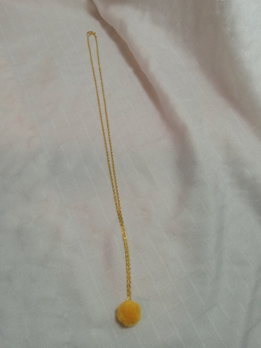 Handmade necklace with a small pom-pom and gold-colored accent hooks and chains
